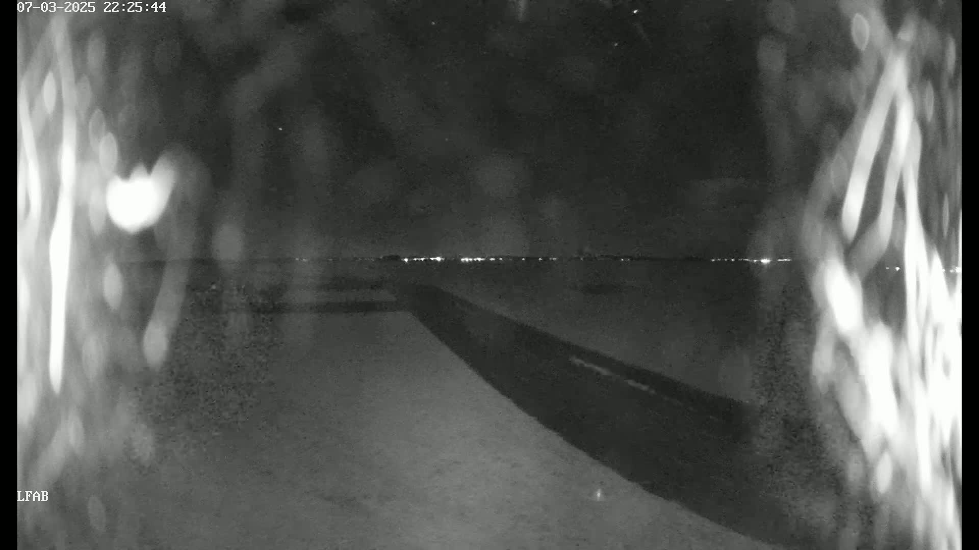 A nighttime, low-light image shows a dark surface leading to a distant horizon with faint lights.