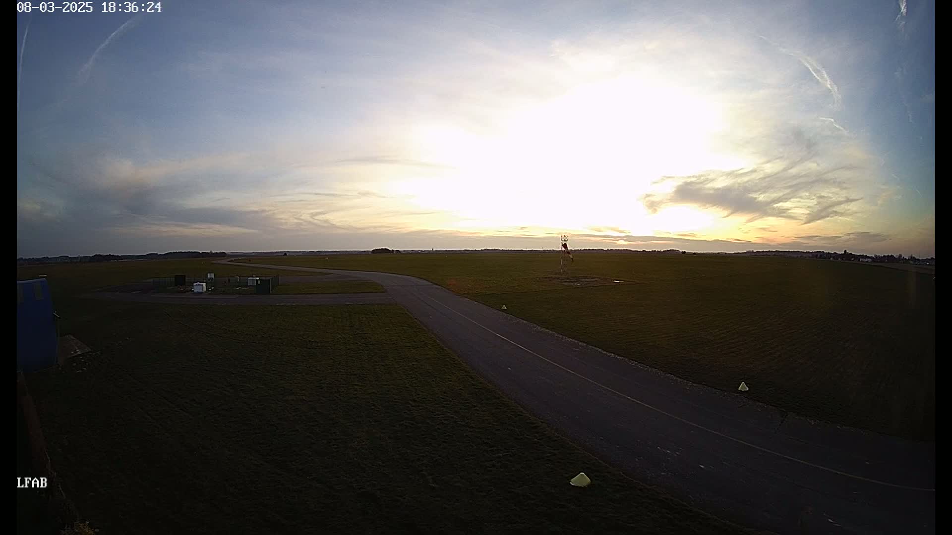 A paved taxiway winds through a grassy airfield at sunset under a partly cloudy sky.