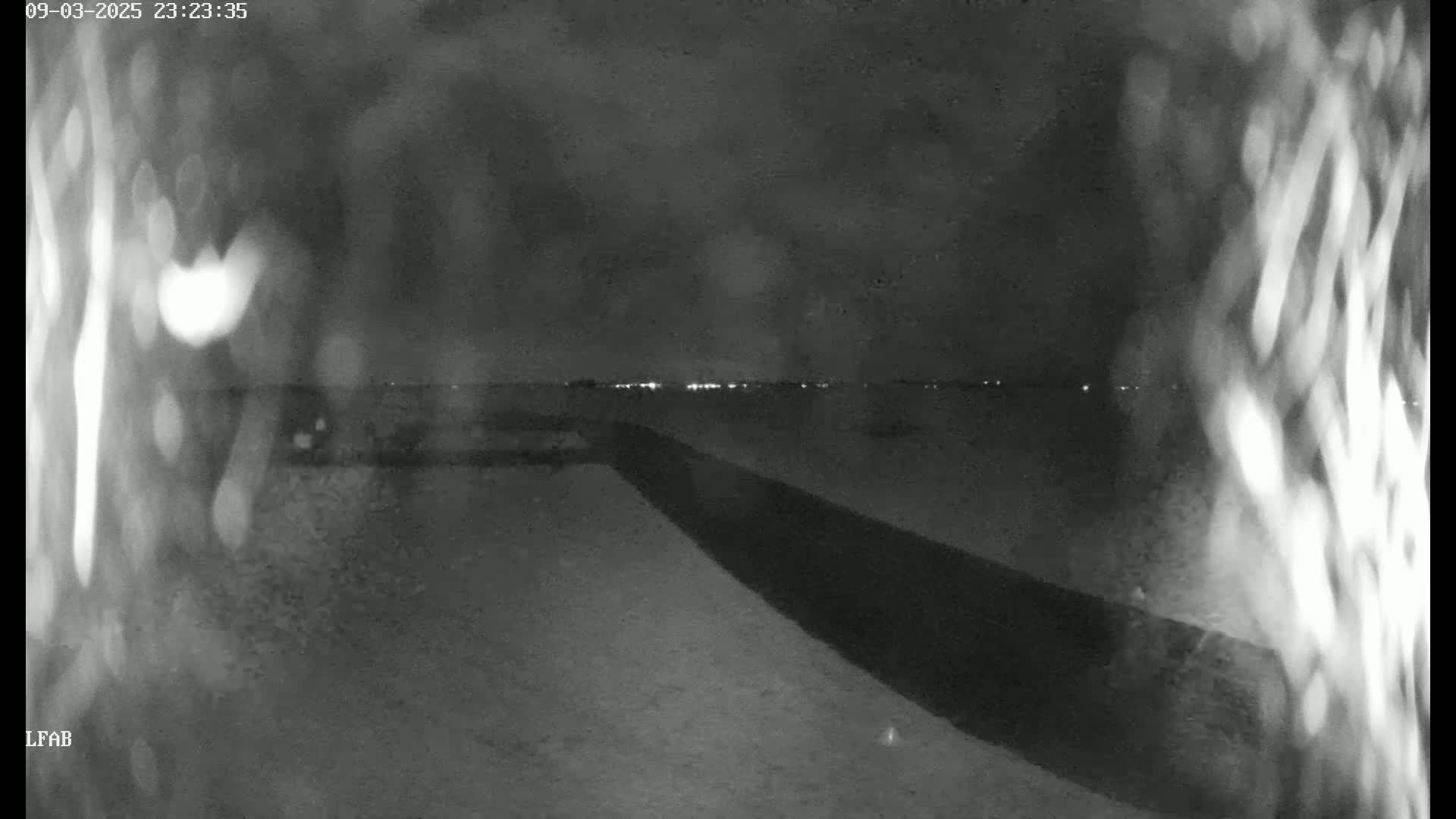 A nighttime, blurry view shows a dark, paved area leading to a distant horizon with faint lights, under a dark, possibly cloudy sky.