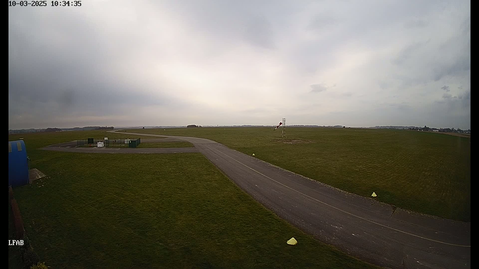 A paved taxiway curves across a grassy airfield under an overcast sky.