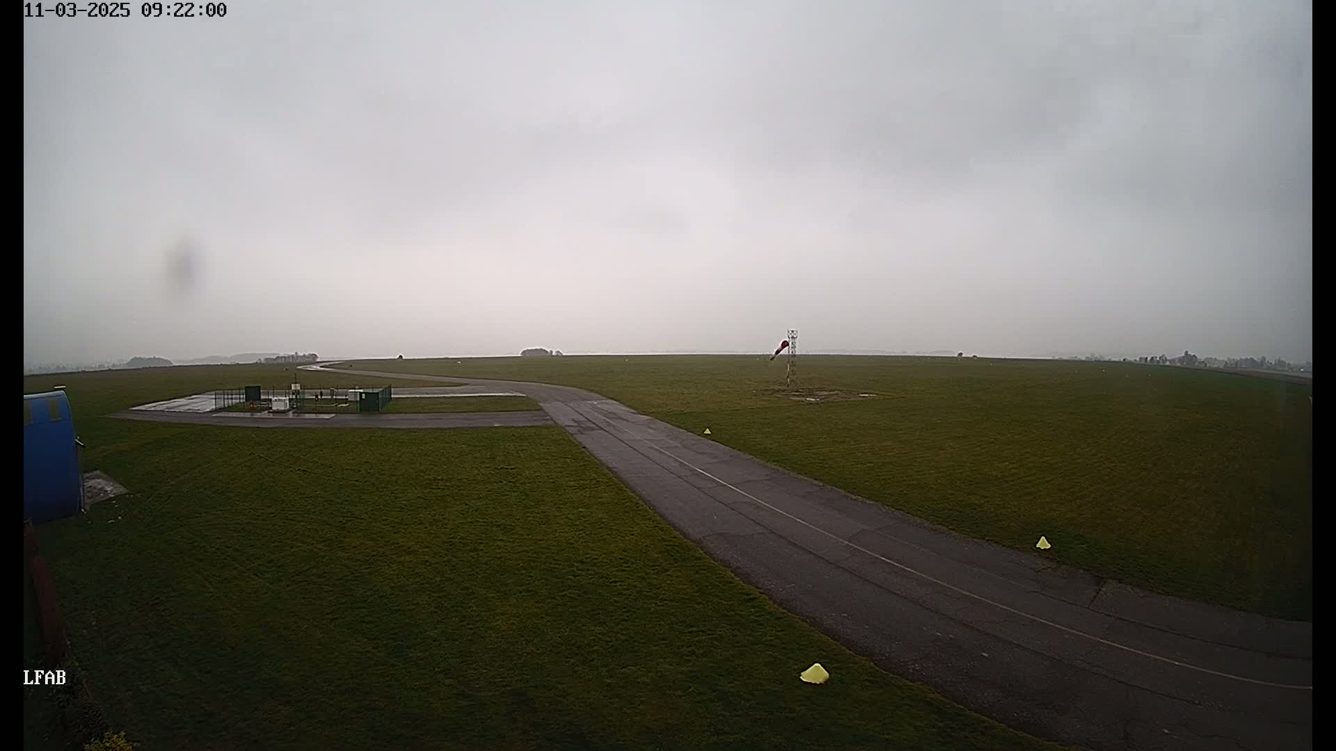 A paved taxiway curves across a grassy airfield under an overcast sky.