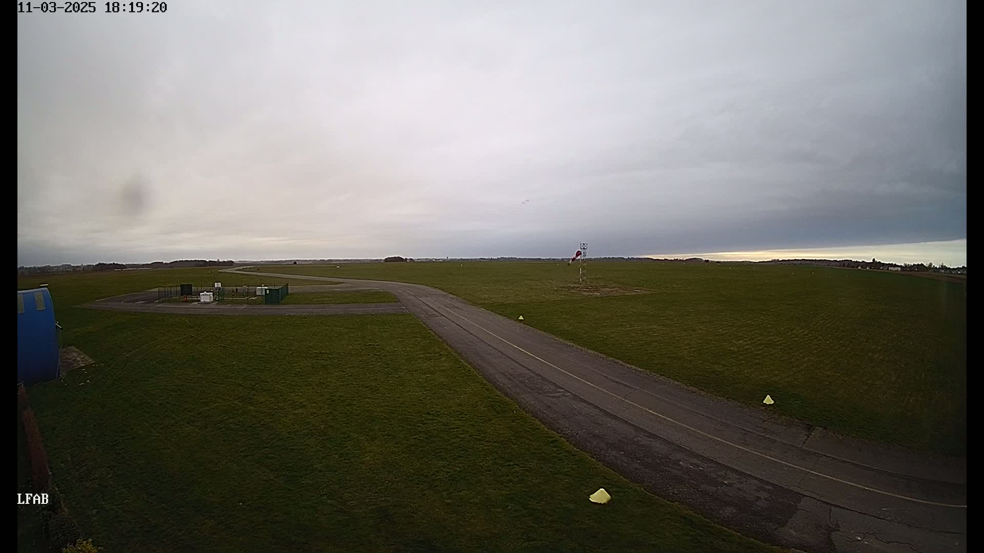 A paved taxiway curves through a grassy airfield under an overcast sky.