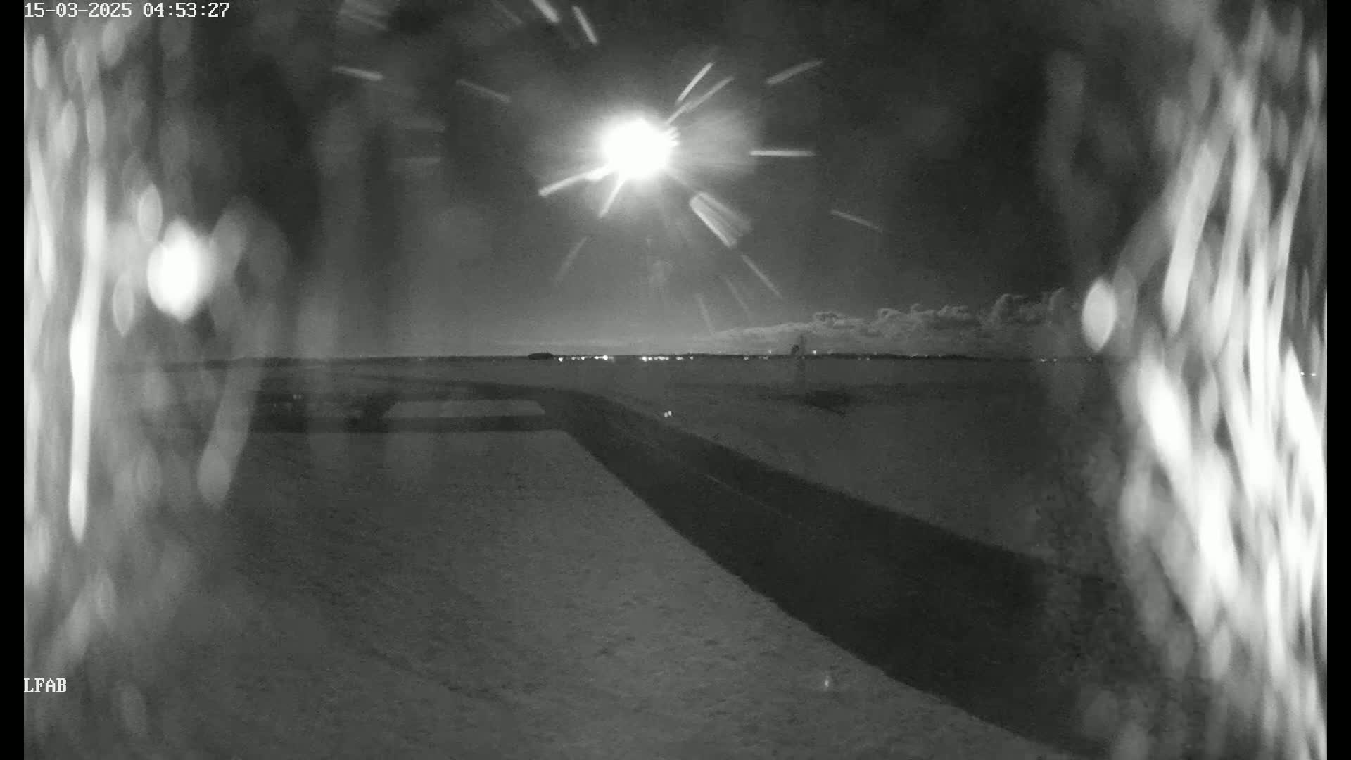A bright light, possibly the sun or moon, shines in a night sky over a snow-covered landscape with a dark road.