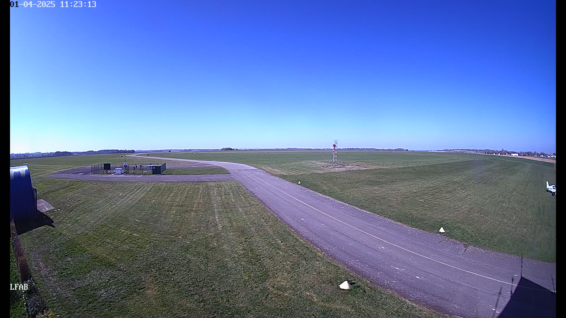 A paved taxiway curves through a grassy airfield under a clear blue sky.