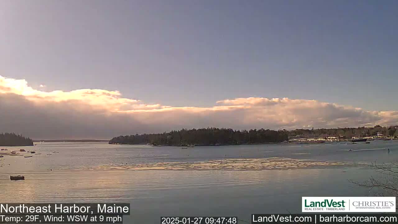 A calm harbor with a few boats and an island in the distance under a partly cloudy sky, with a light wind.