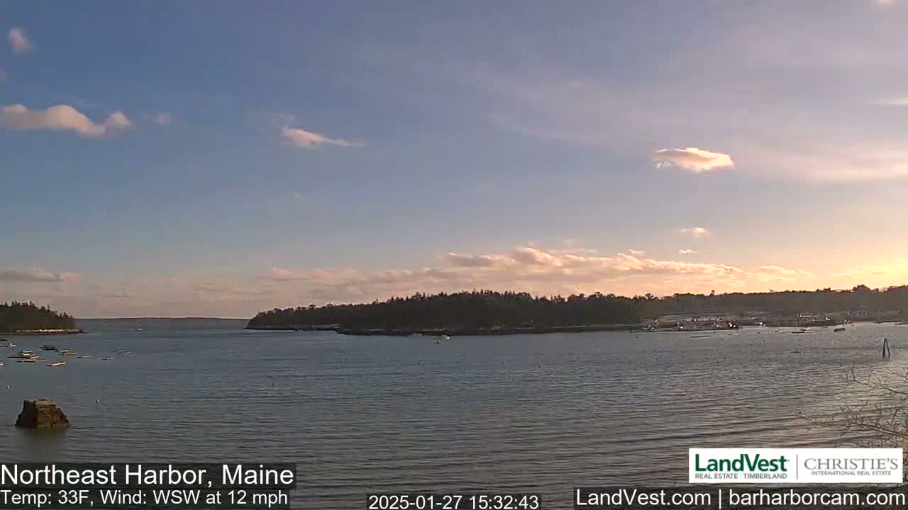A calm harbor with a few boats is seen under a partly cloudy sky at sunset, with a light wind.