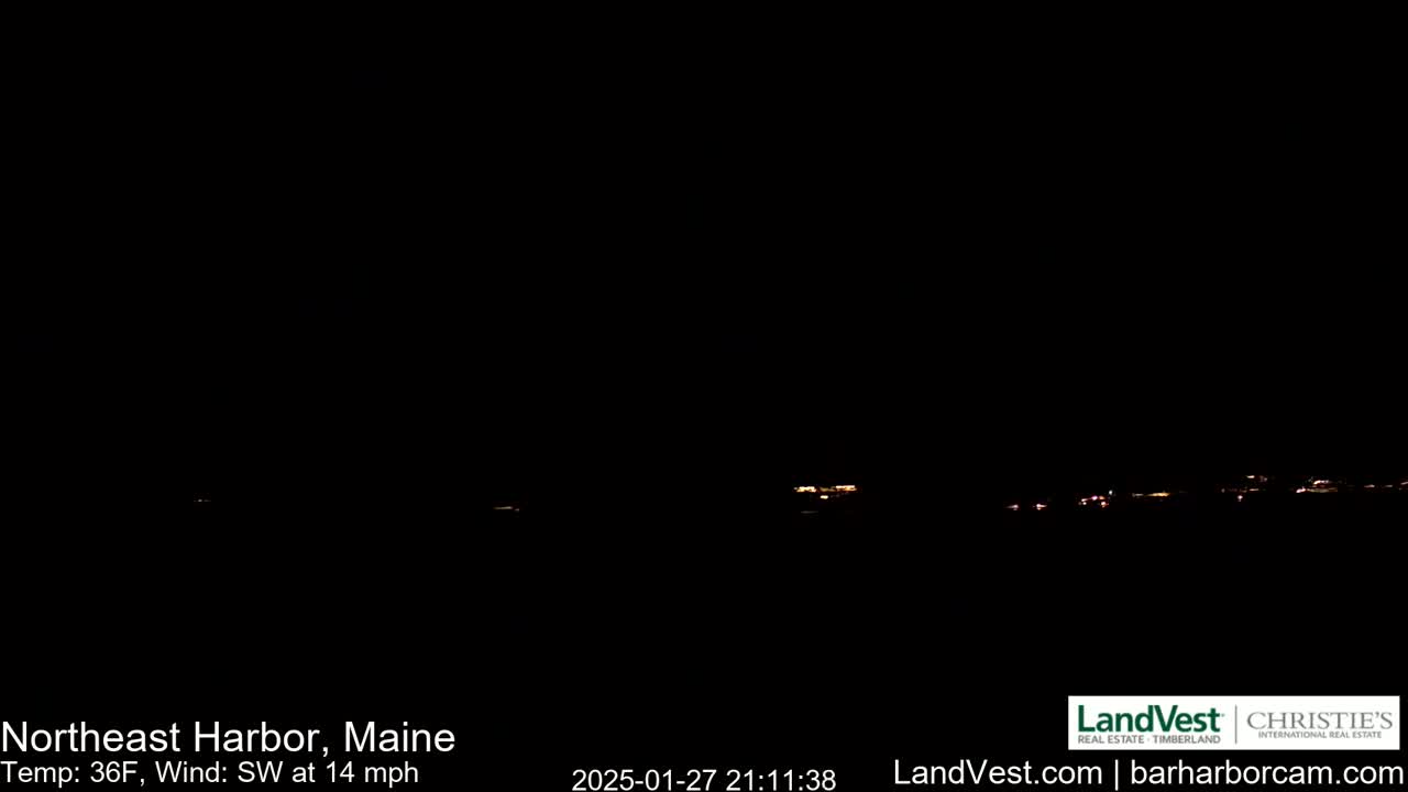 A nighttime long shot of a dark landscape shows a few distant lights under a dark sky with a southwest wind of 14 mph and a temperature of 36°F.