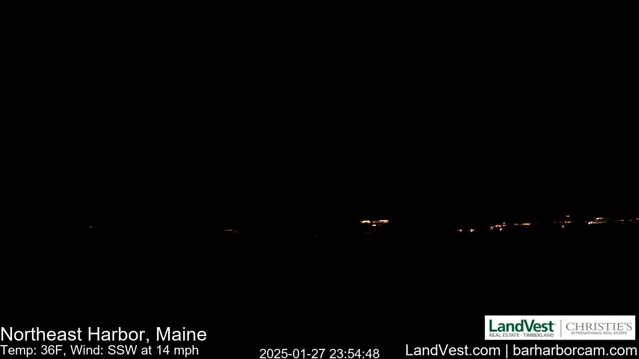 A nighttime long shot shows a dimly lit town on the horizon under a dark, clear sky with a 14 mph southwest wind and a temperature of 36°F.