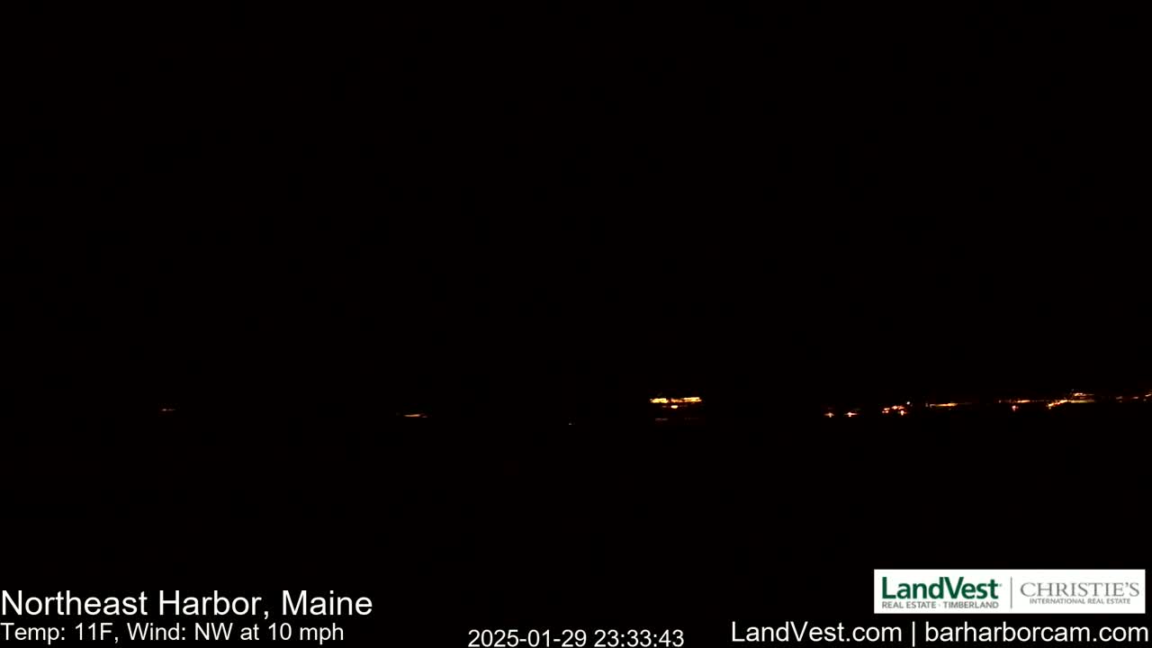A nighttime long shot shows a distant line of faint, orange-yellow lights against a completely black sky, with a northwest wind blowing at 10 mph and a temperature of 11°F.