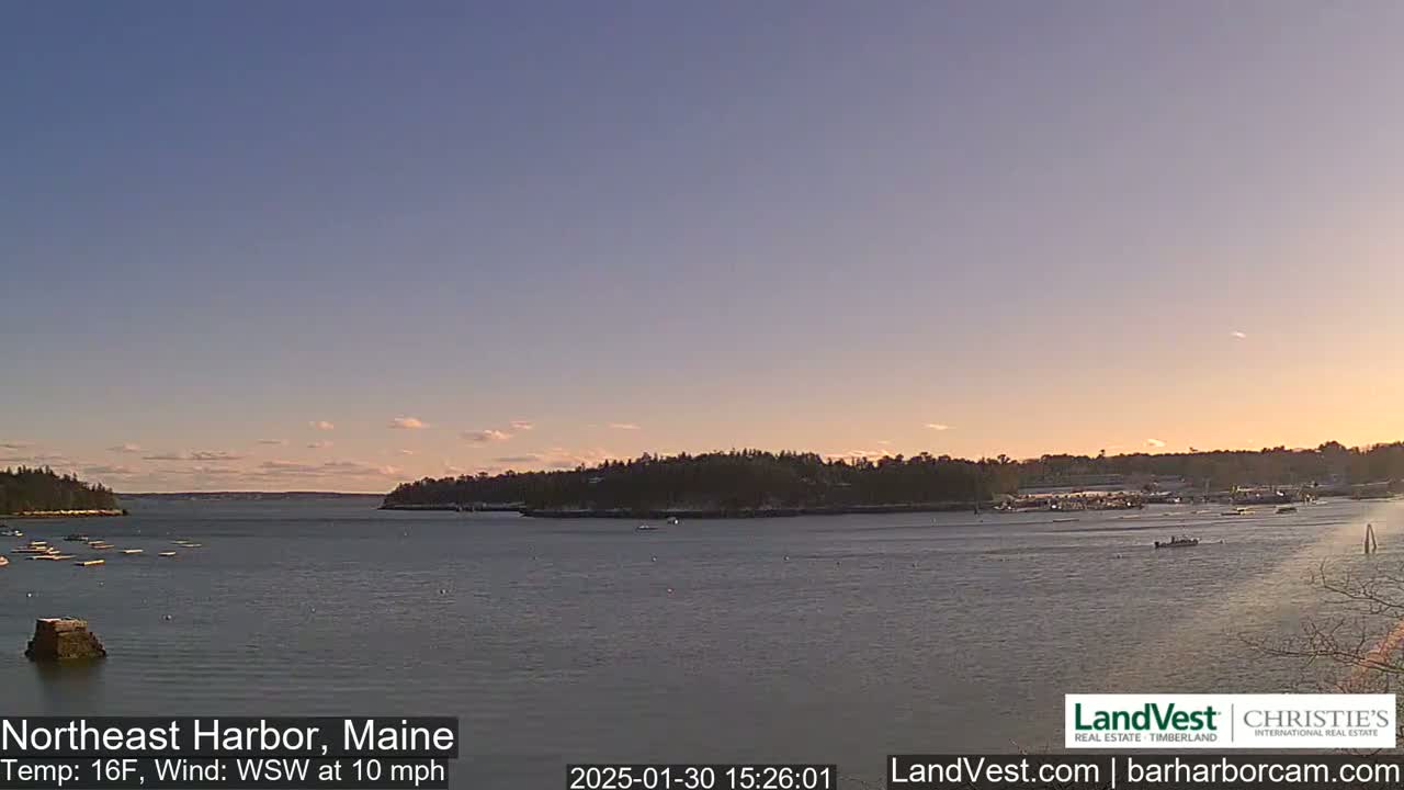 A calm harbor at sunset, with a few boats and snow-dusted land in the background, under a clear sky.