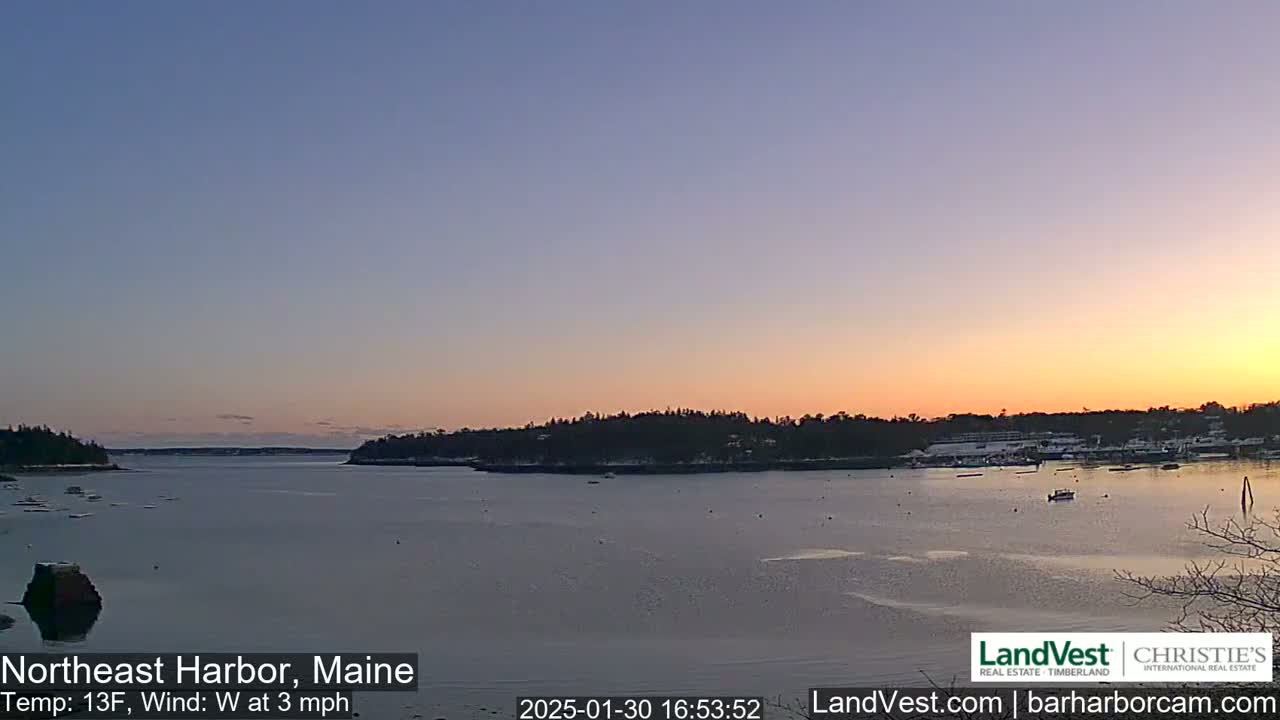A calm, partially frozen bay at sunset, under a clear, pale orange and purple sky, with a gentle westerly wind.