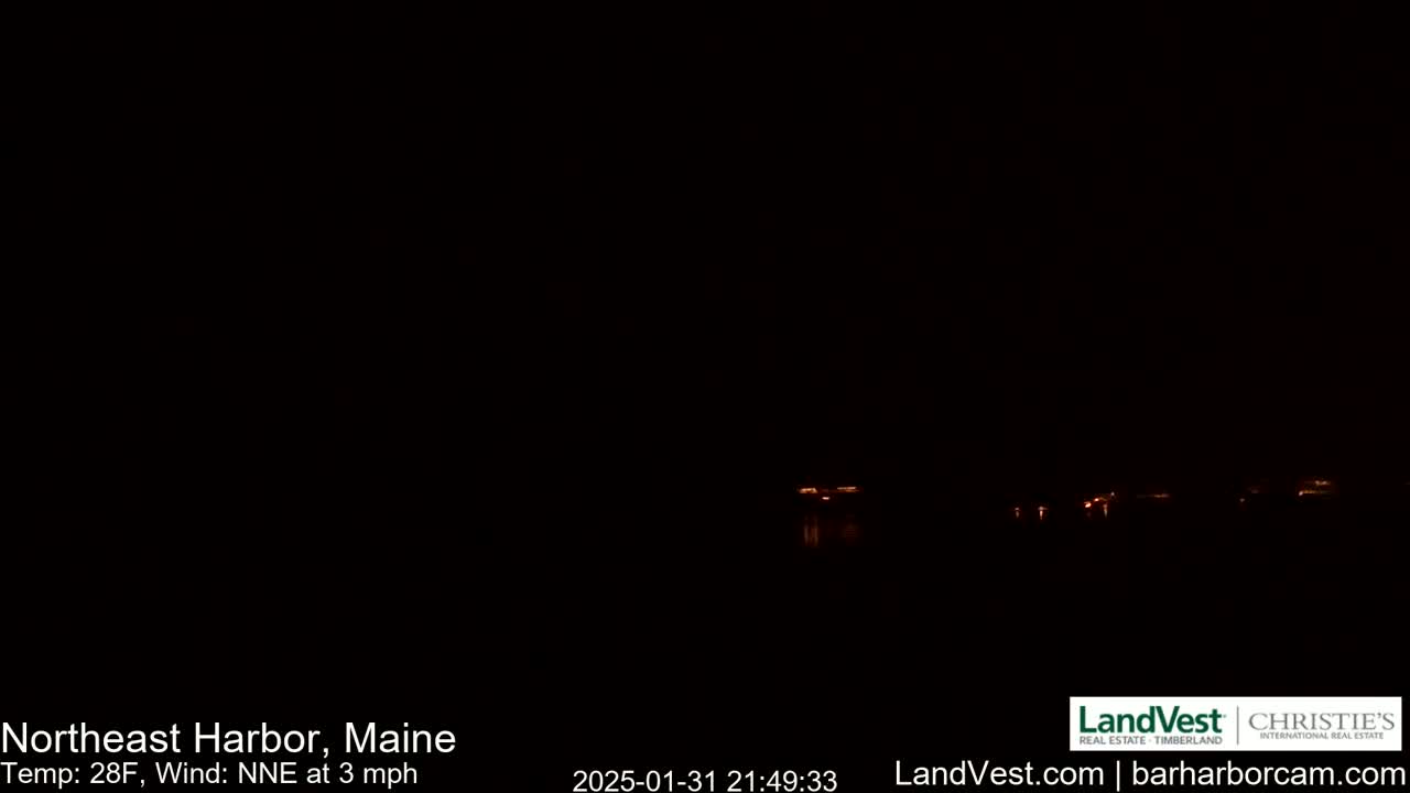 A dark, nighttime view of a body of water with faintly visible lights across the horizon under a clear, dark sky, with a temperature of 28°F and a north-northeast wind at 3 mph.