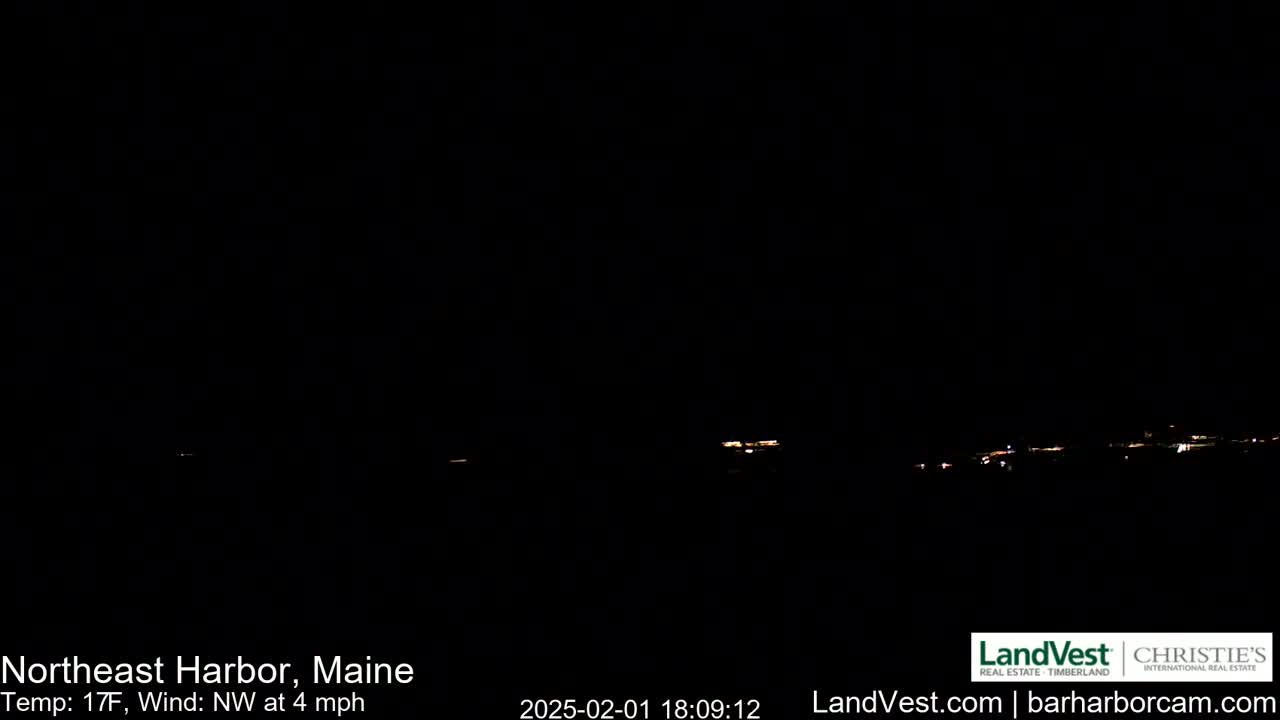 A nighttime, long-distance view of faintly lit buildings under a dark sky with a northwest wind of 4 mph and a temperature of 17 degrees Fahrenheit.