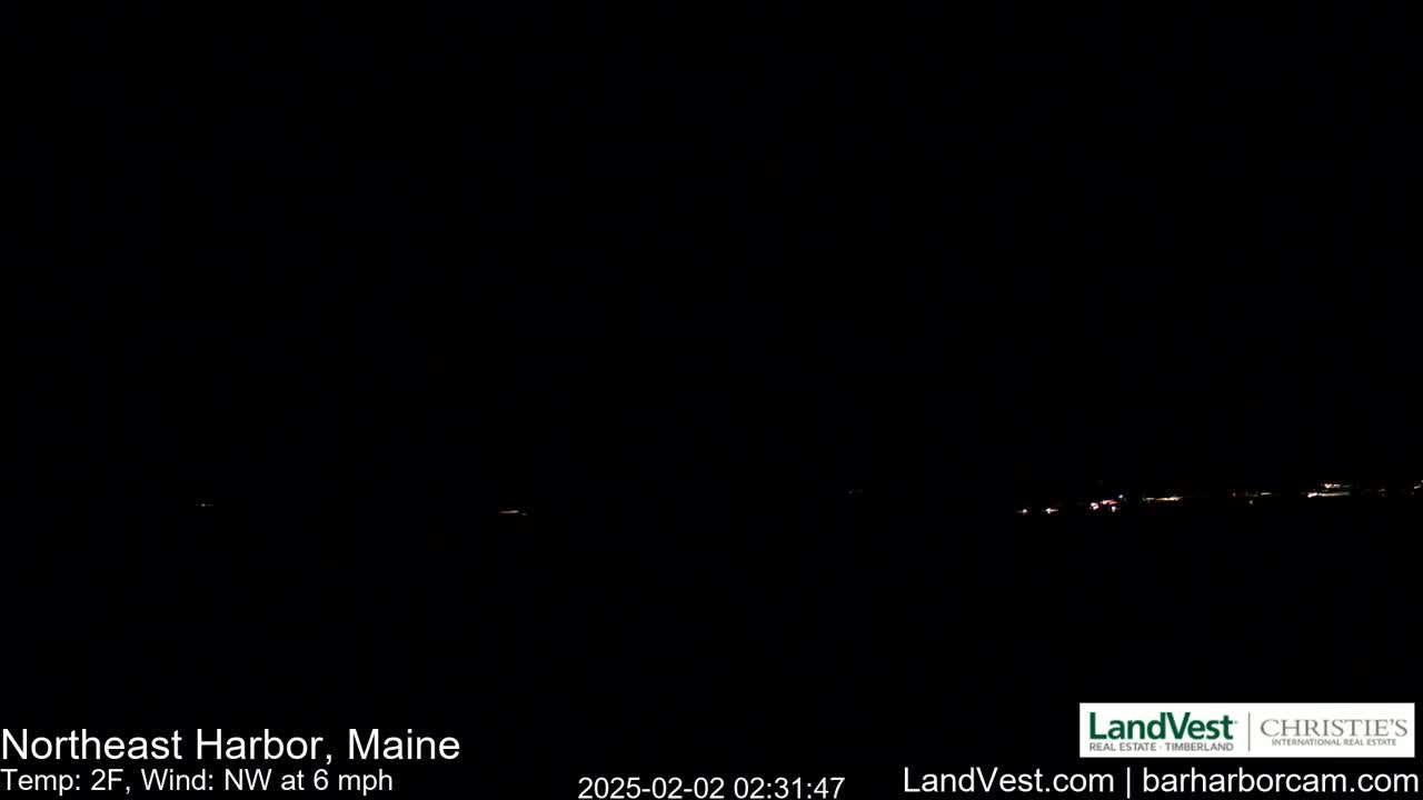 A dark, nighttime scene shows a distant line of faint lights across a dark horizon under a clear, black sky with a temperature of 2°F and a northwest wind at 6 mph.