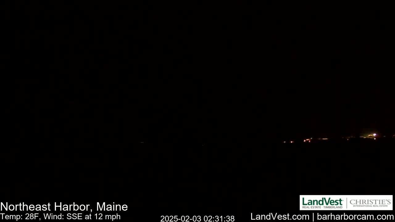 A dark nighttime scene shows a dimly lit horizon with a few distant lights under a clear, dark sky, with a 28°F temperature and a 12 mph wind from the south-southeast.