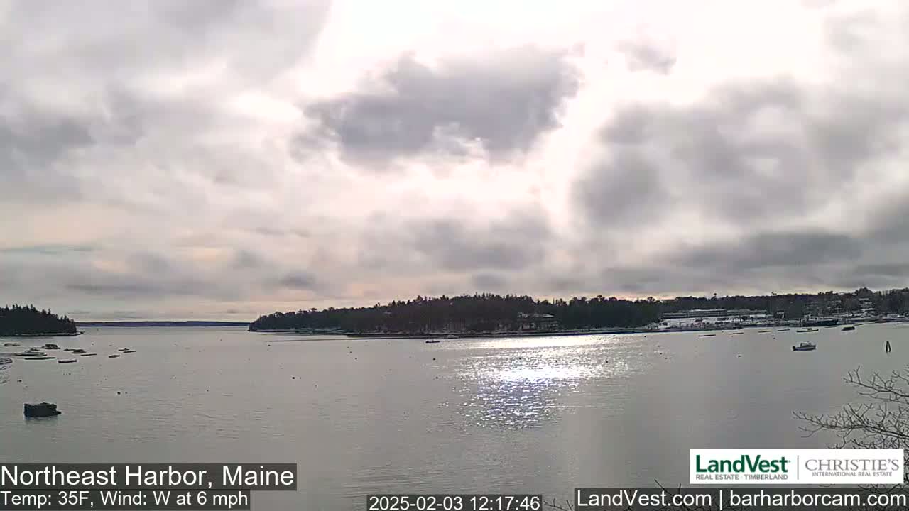 A partly cloudy day with a west wind at 6 mph shows a calm harbor with boats and a snow-dusted shoreline.