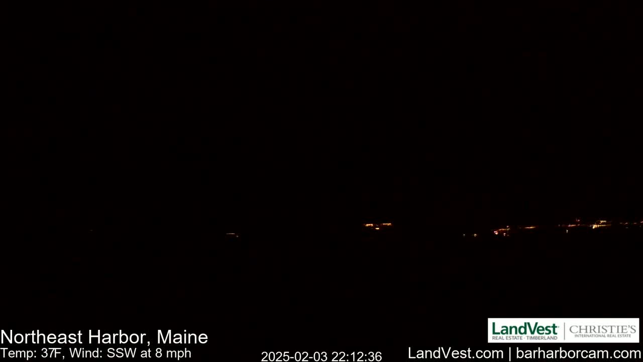 A dark, nighttime view of a dimly lit town across a body of water, with a 37°F temperature and an 8 mph south-southwest wind.