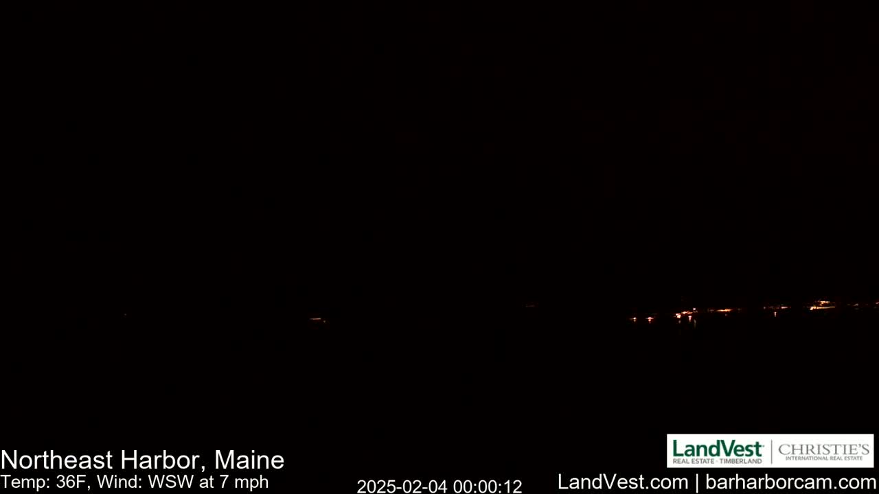 A dark, nighttime scene shows a faint line of distant lights across a dark horizon under a clear, dark sky with a 36°F temperature and a 7 mph wind from the west-southwest.