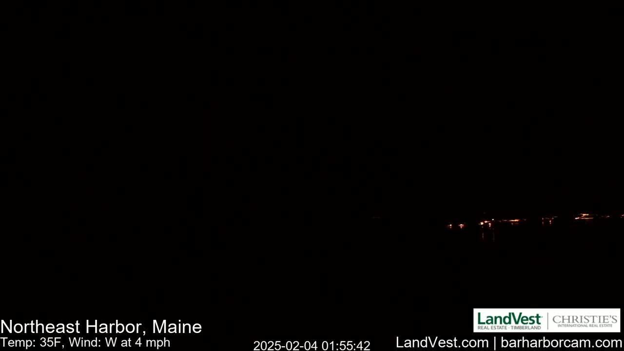 A nighttime long shot shows a dark, mostly black scene with a faint line of distant lights on the horizon, under a dark sky, with a 35°F temperature and a 4 mph west wind.