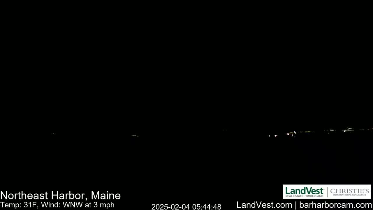 A nighttime, long-range view of a dimly lit town or coastline under a dark sky with a 31°F temperature and a light WNW wind at 3 mph.
