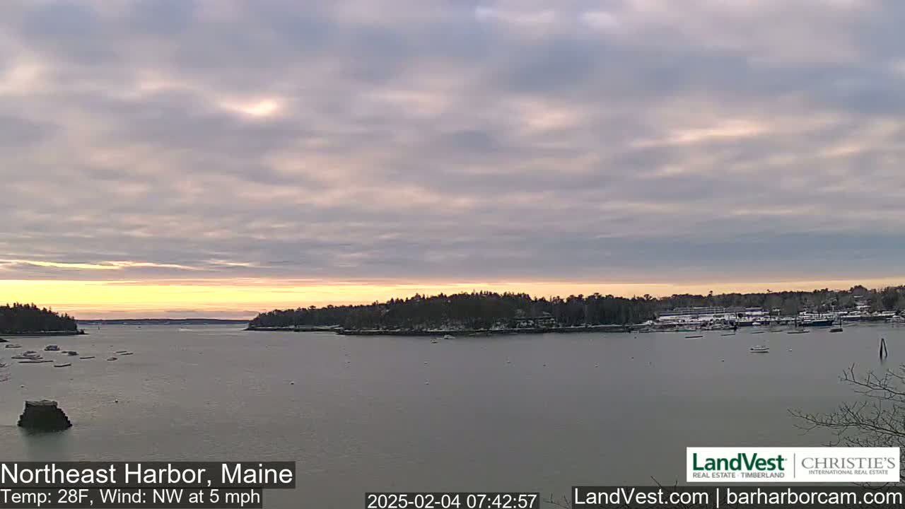 A calm harbor at sunrise under a mostly cloudy sky with a light northwest wind.