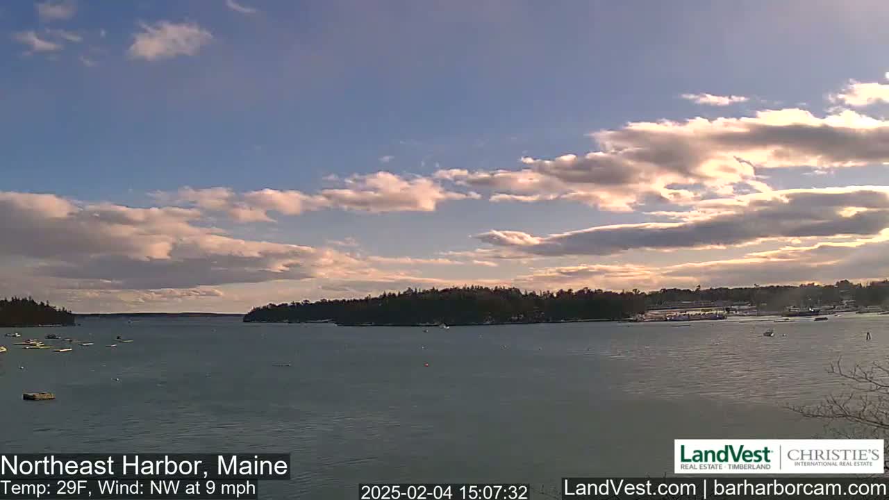 A partly cloudy afternoon scene overlooks a calm harbor with a few boats, under a mostly clear sky with a light northwest wind.