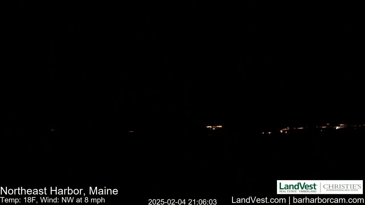 A dark nighttime scene shows a distant line of faint lights across a black horizon under a clear, dark sky with an 18°F temperature and a northwest wind at 8 mph.