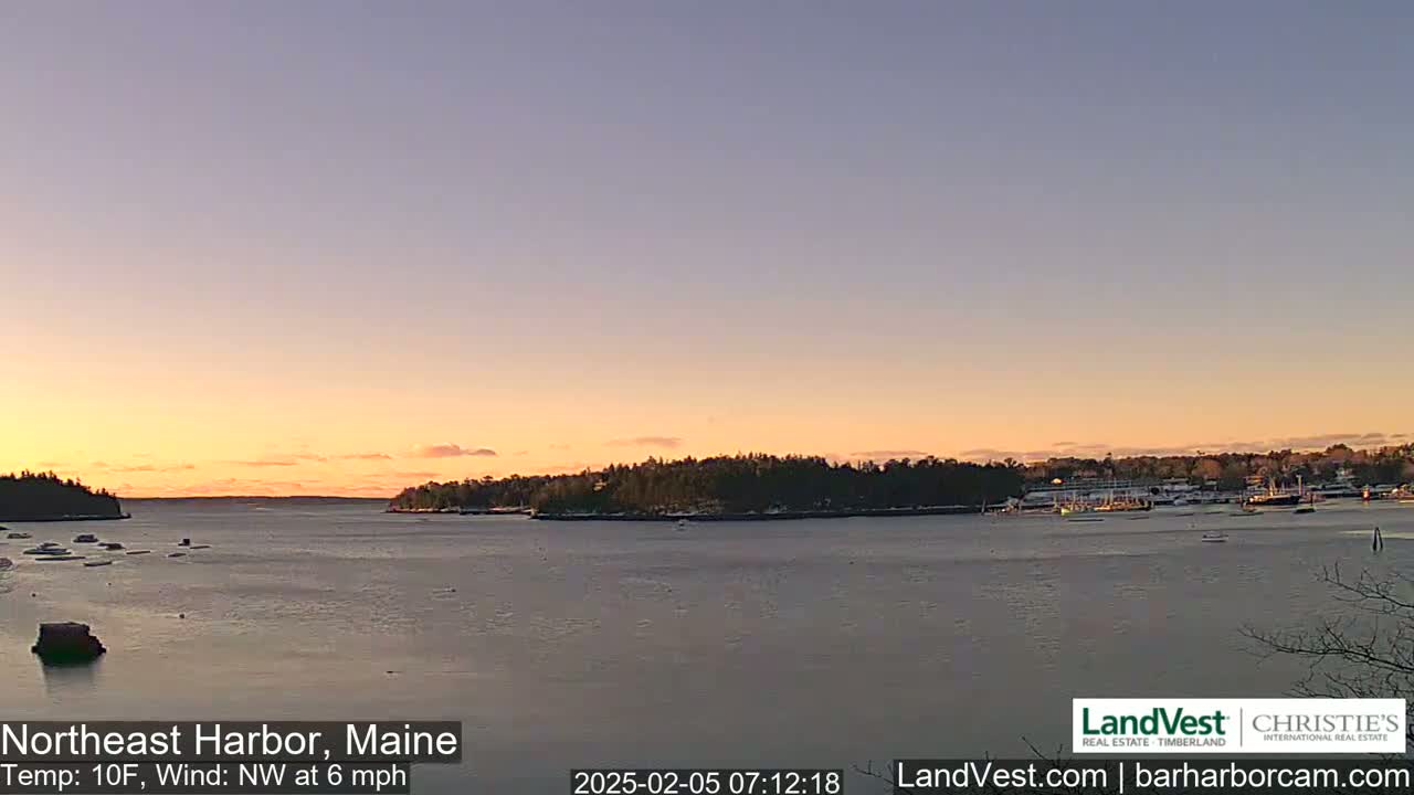 A calm harbor at sunset with a partly frozen waterway, under a pale orange and pink sky, and a light northwest wind.