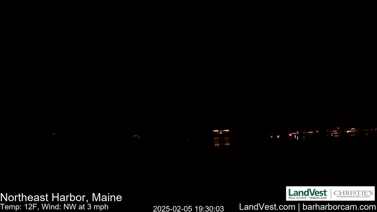 A nighttime view of a dark body of water with faint lights across the horizon under a clear, dark sky, with a temperature of 12°F and a northwest wind of 3 mph.