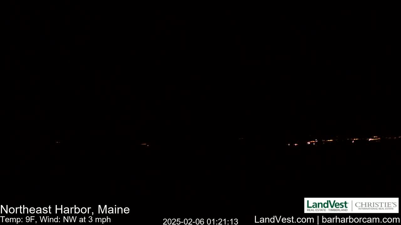A nighttime long shot shows a dark landscape with a faint line of distant lights under a clear, dark sky, with a temperature of 9°F and a northwest wind of 3 mph.