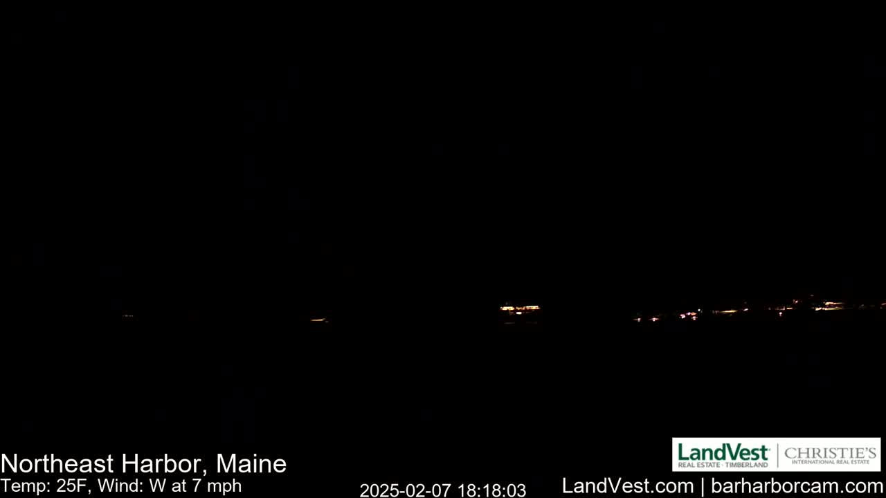 A dark, nighttime scene shows a distant line of faintly lit buildings under a clear, dark sky with a temperature of 25°F and a 7 mph westerly wind.