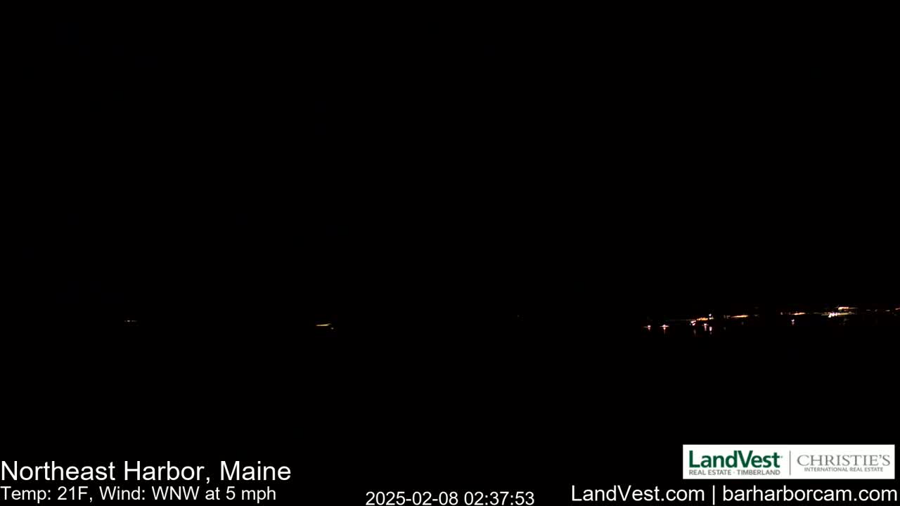 A dark nighttime scene shows a faint, distant line of lights across the horizon, with a 21°F temperature and a 5 mph wind from the west-northwest.