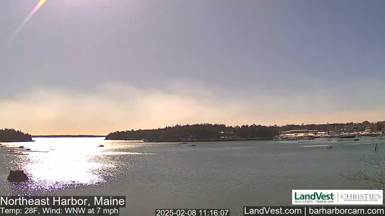 A calm body of water reflects sunlight, with a small town and trees visible on the shore in a 28°F, 7 mph WNW wind.
