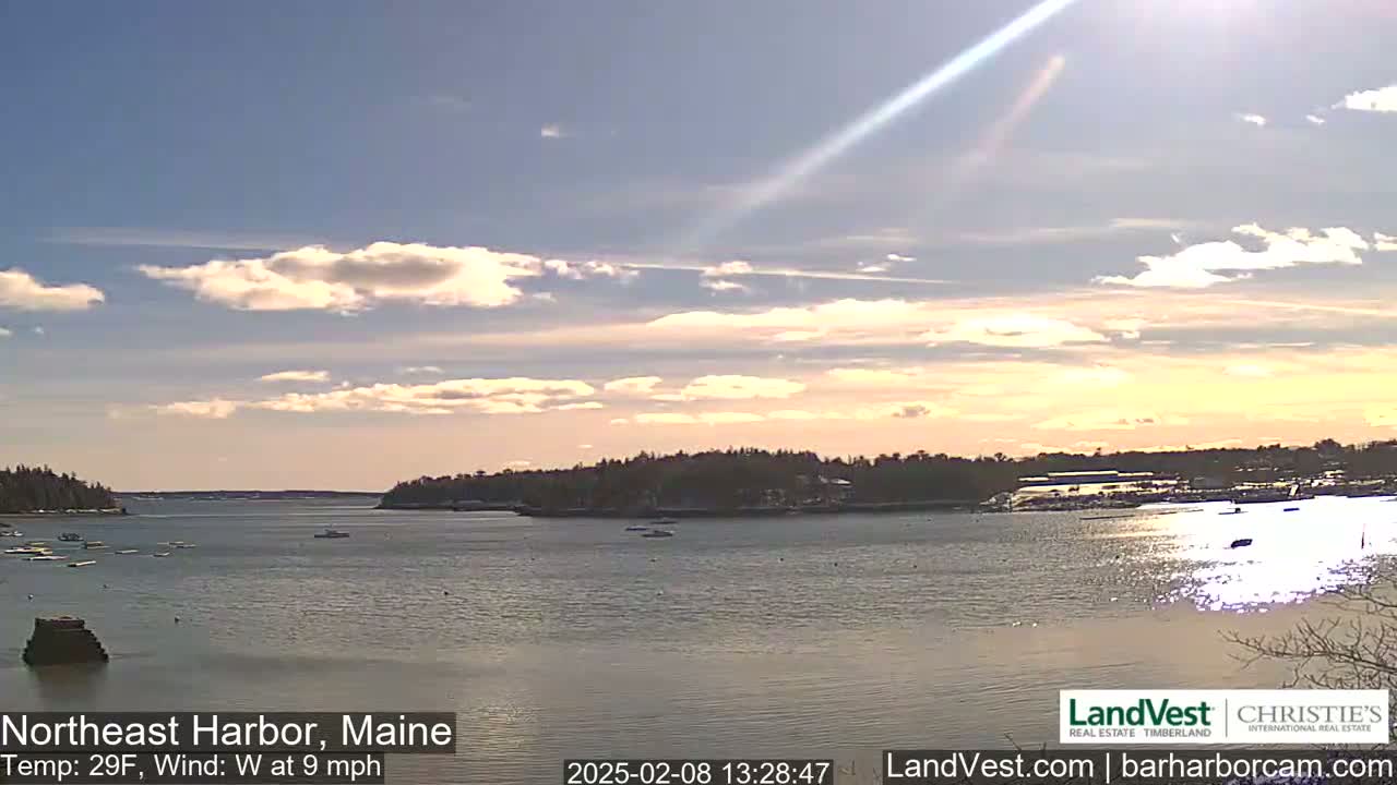 A partly cloudy, calm day on a harbor with a few boats, featuring land on both sides.