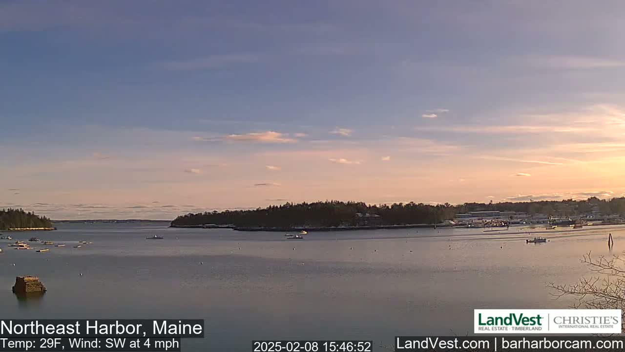 A calm harbor with a few boats is seen at sunset under a mostly clear sky, with a light southwest wind.