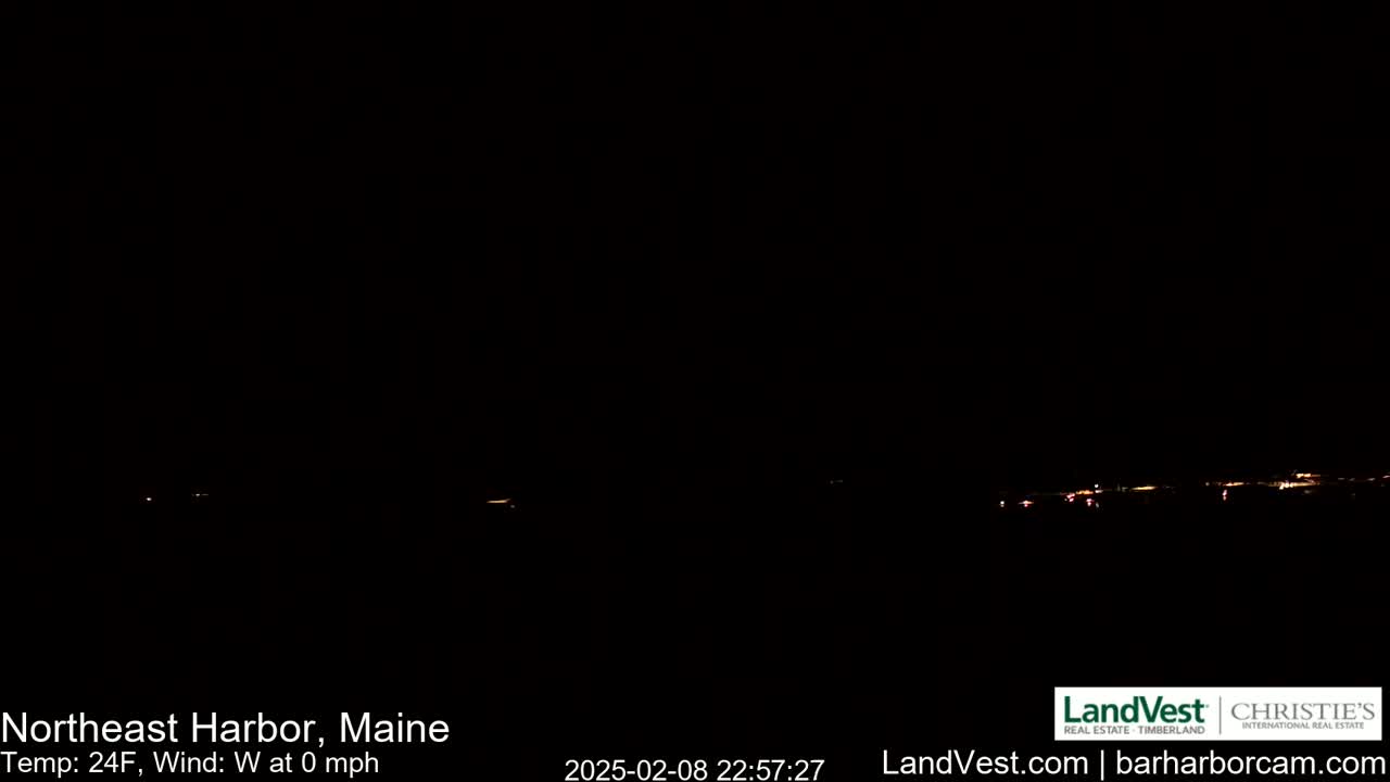 A dark, nighttime view of a distant, faintly lit shoreline under a clear, calm sky with a temperature of 24°F.