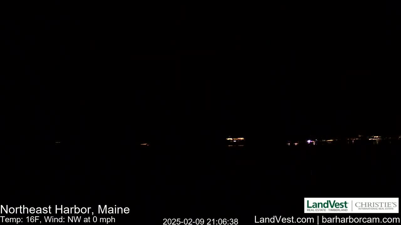 A nighttime, dark scene shows a distant, dimly lit shoreline across a body of water, with a calm, 0 mph northwest wind and 16°F temperature.
