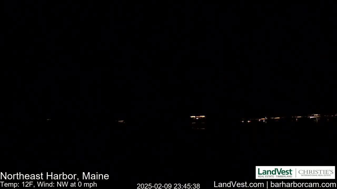 A dark nighttime scene shows a faint, distant line of lights across a body of water, with a calm, 12-degree Fahrenheit windless night.