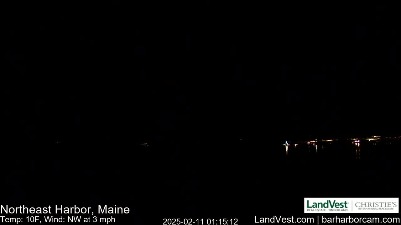 A dark, nighttime view of a calm body of water with faintly visible lights on the far shore under a clear sky, a 10°F temperature and a northwest wind of 3 mph.