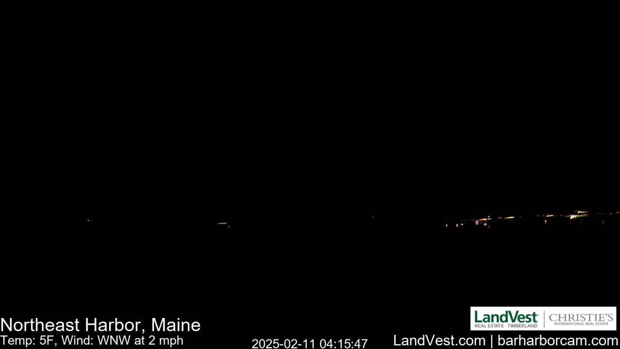 A nighttime long shot shows a dark, dimly lit horizon with a few distant lights under a clear, dark sky; the temperature is 5°F, and the wind is blowing from the west-northwest at 2 mph.
