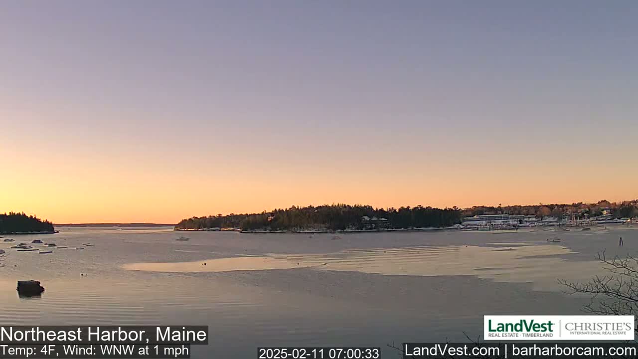 A partly frozen harbor at sunrise, under a pale orange and lavender sky, with a light wind.