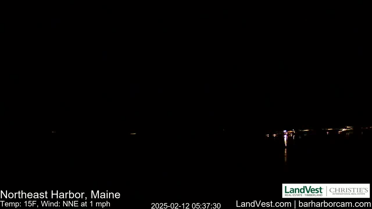 A nighttime, low-light view of a dark body of water with faintly visible lights across the horizon under a dark sky, with a temperature of 15°F and a north-northeast wind of 1 mph.
