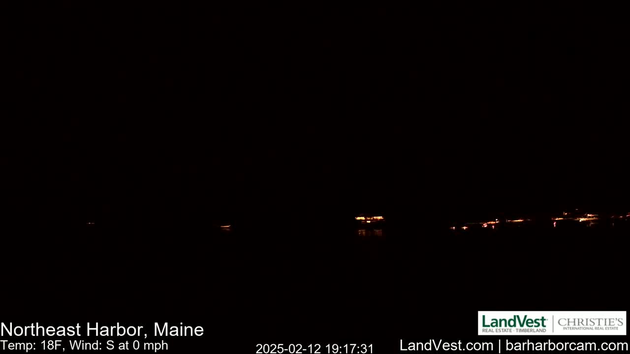 A nighttime, dark view of faintly illuminated lights across a body of water, under calm, 18-degree Fahrenheit weather.