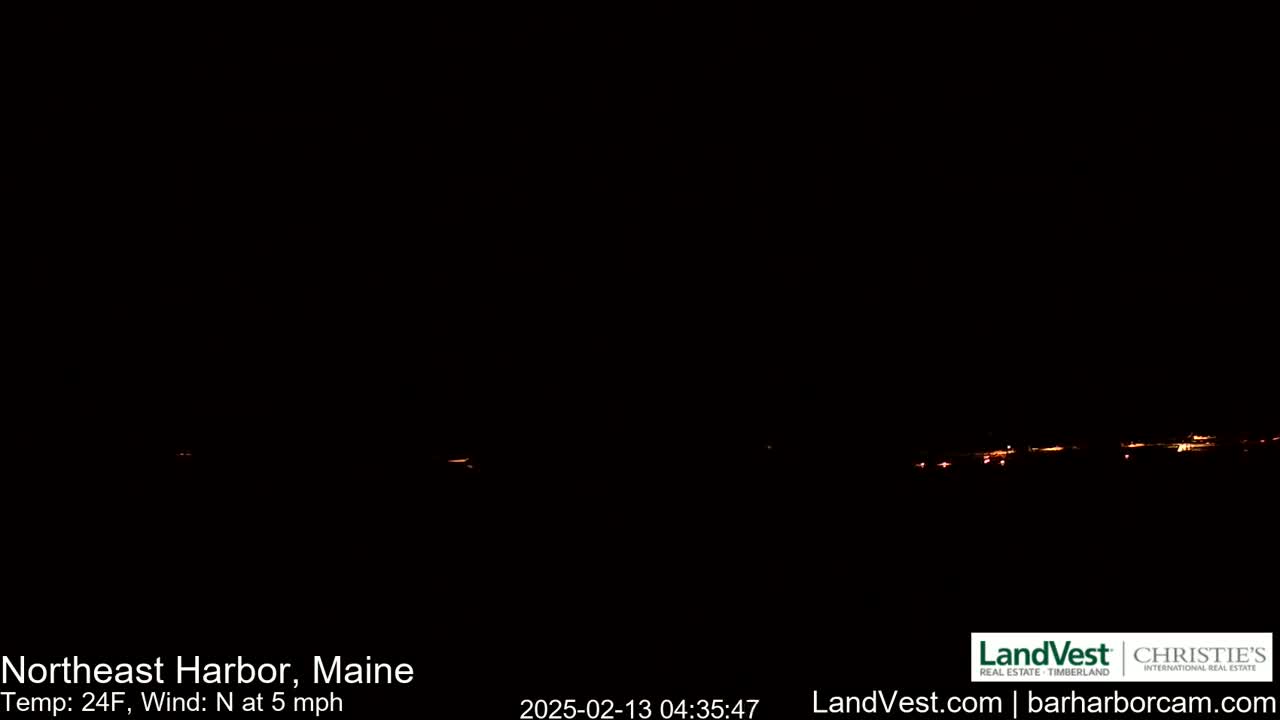 A nighttime long shot shows a distant line of faint, orange lights on the horizon under a dark, clear sky with a northerly wind of 5 mph and a temperature of 24°F.