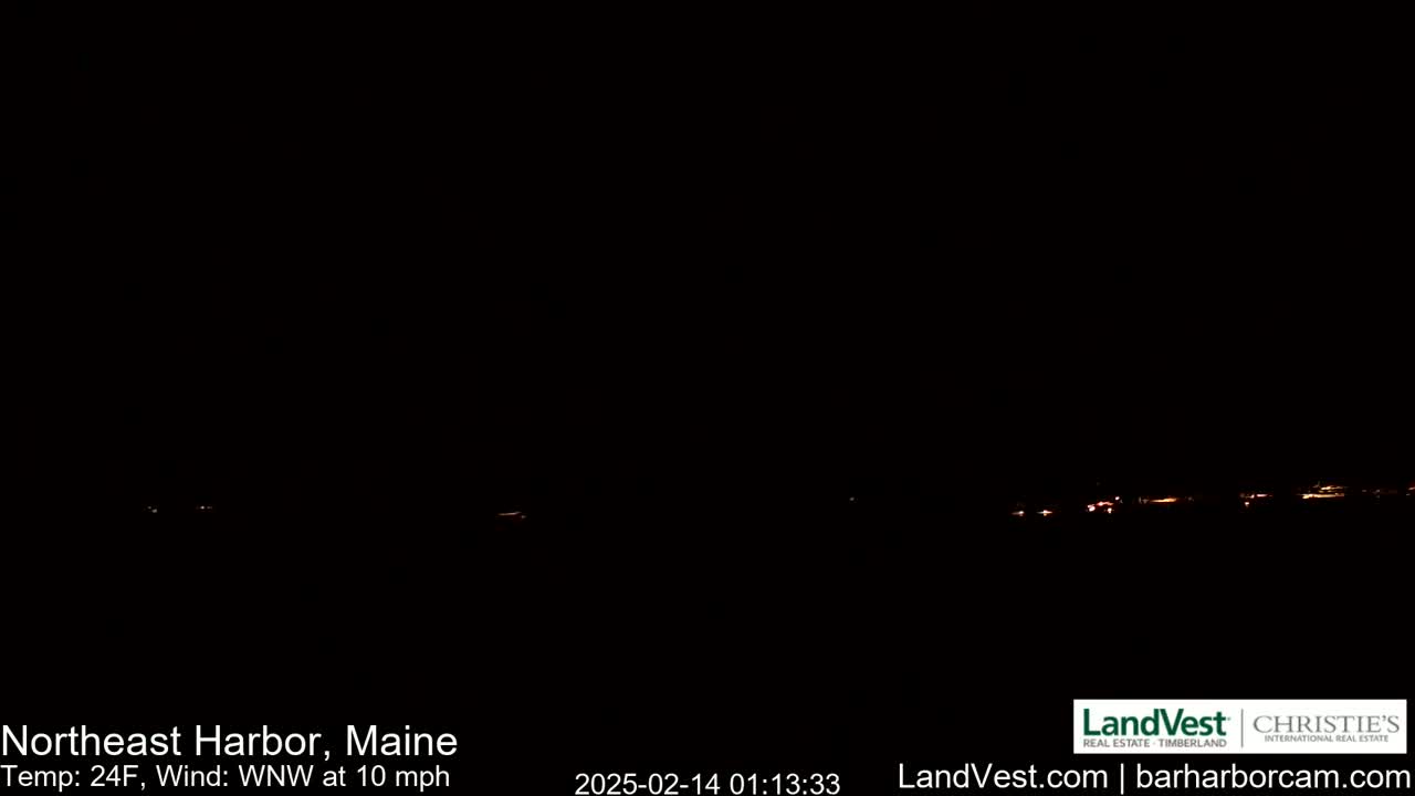 A dark nighttime scene shows a faint line of distant lights on the horizon under a clear, dark sky.