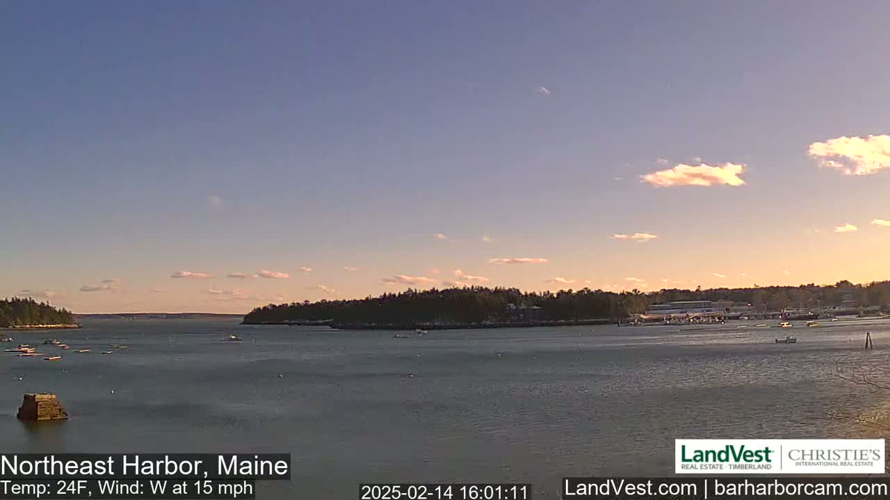 A calm harbor with a few boats is seen under a partly cloudy, dusky sky.