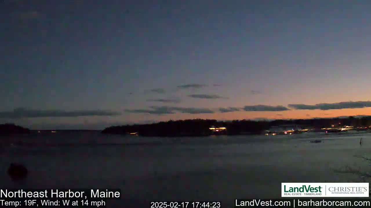 A dark, calm body of water is visible at dusk under a mostly clear sky with a few clouds, with faintly lit landmasses on either side of it.