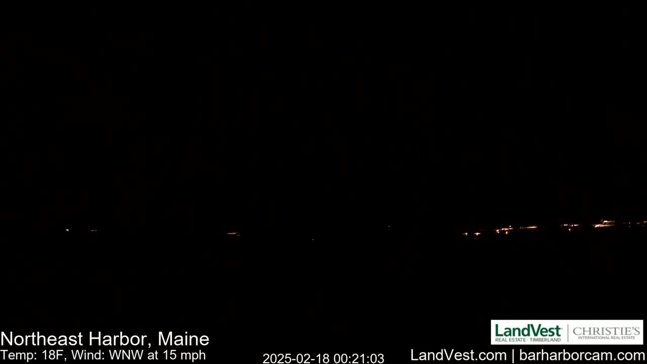 A nighttime, long shot of a dimly lit town on the horizon, under a dark sky with a 15 mph wind from the west-northwest and a temperature of 18°F.