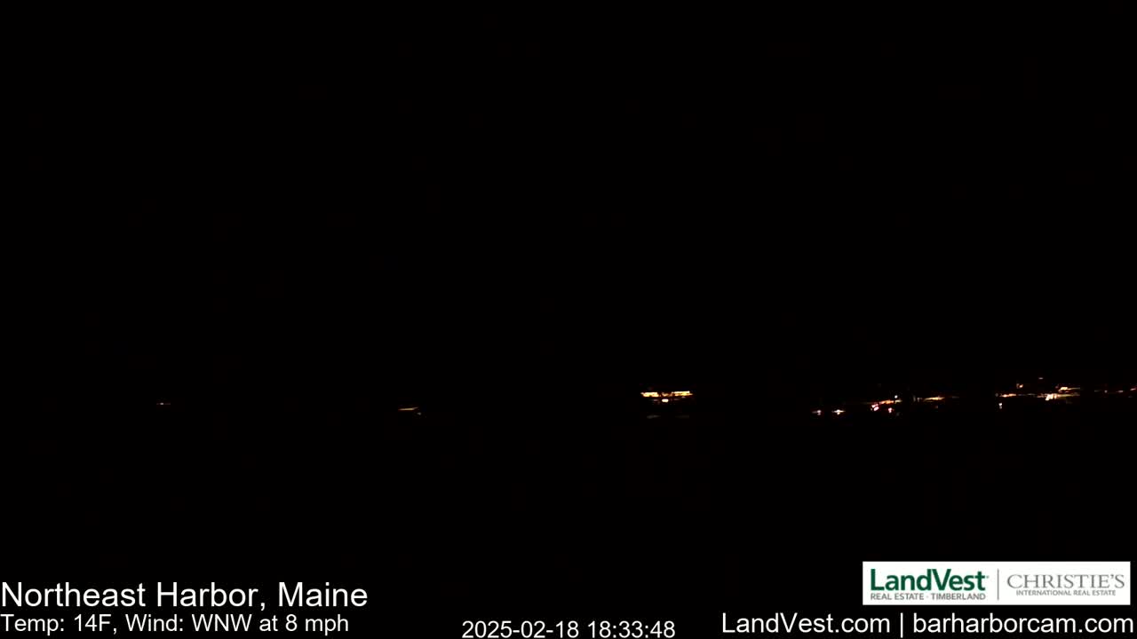 A nighttime long shot shows a dark landscape with faintly visible lights from a distant town under a clear, dark sky.