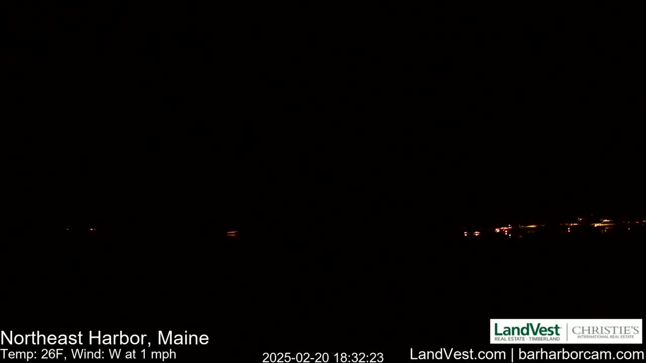 A nighttime long shot shows a dark, low-lit waterfront town under a clear, dark sky with a 26°F temperature and a 1 mph west wind.
